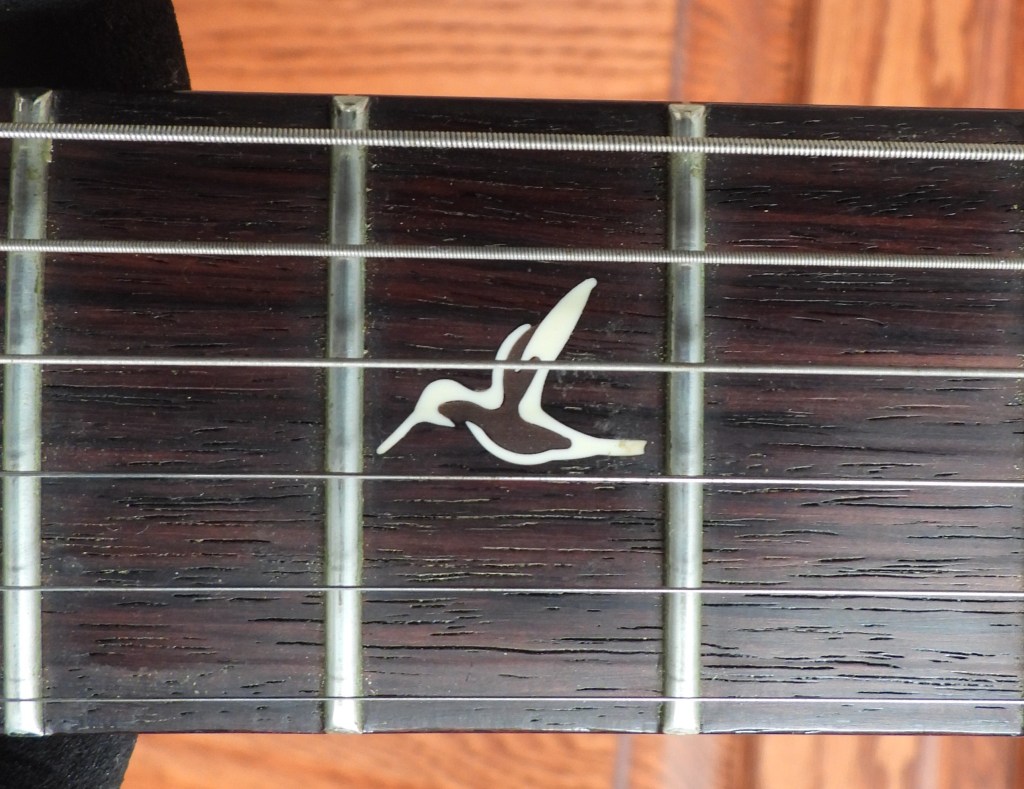 Close-up of dark (rosewood) guitar fretboard with white, hummingbird-shaped inlay.