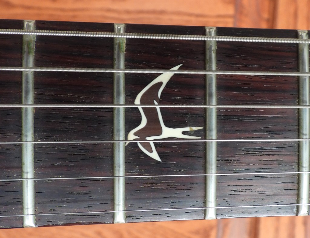 Close-up of dark (rosewood) guitar fretboard with white, tern-shaped inlay.